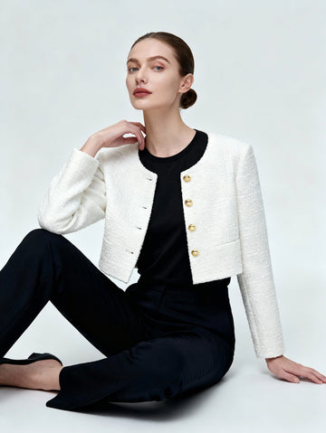 Woman wearing a white jacket with gold buttons over a black outfit on a light gray background