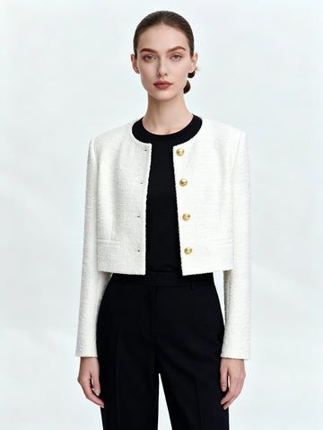 Woman wearing a white jacket with gold buttons over a black top and pants on a light gray background