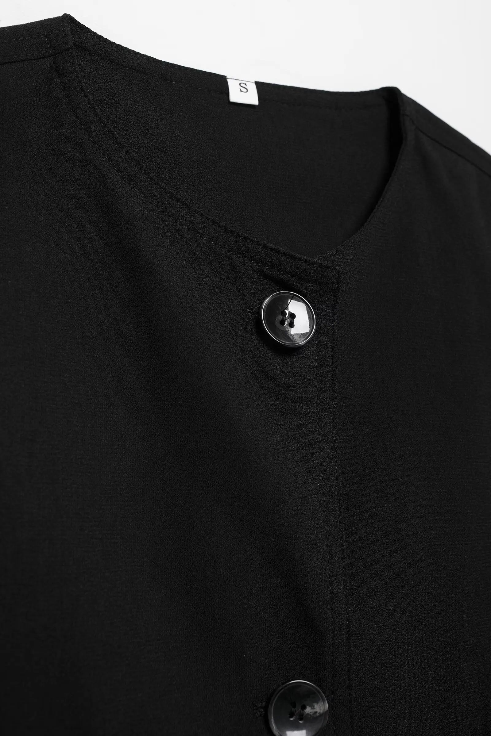 Close-up of a black buttoned garment with a brand label on a white background