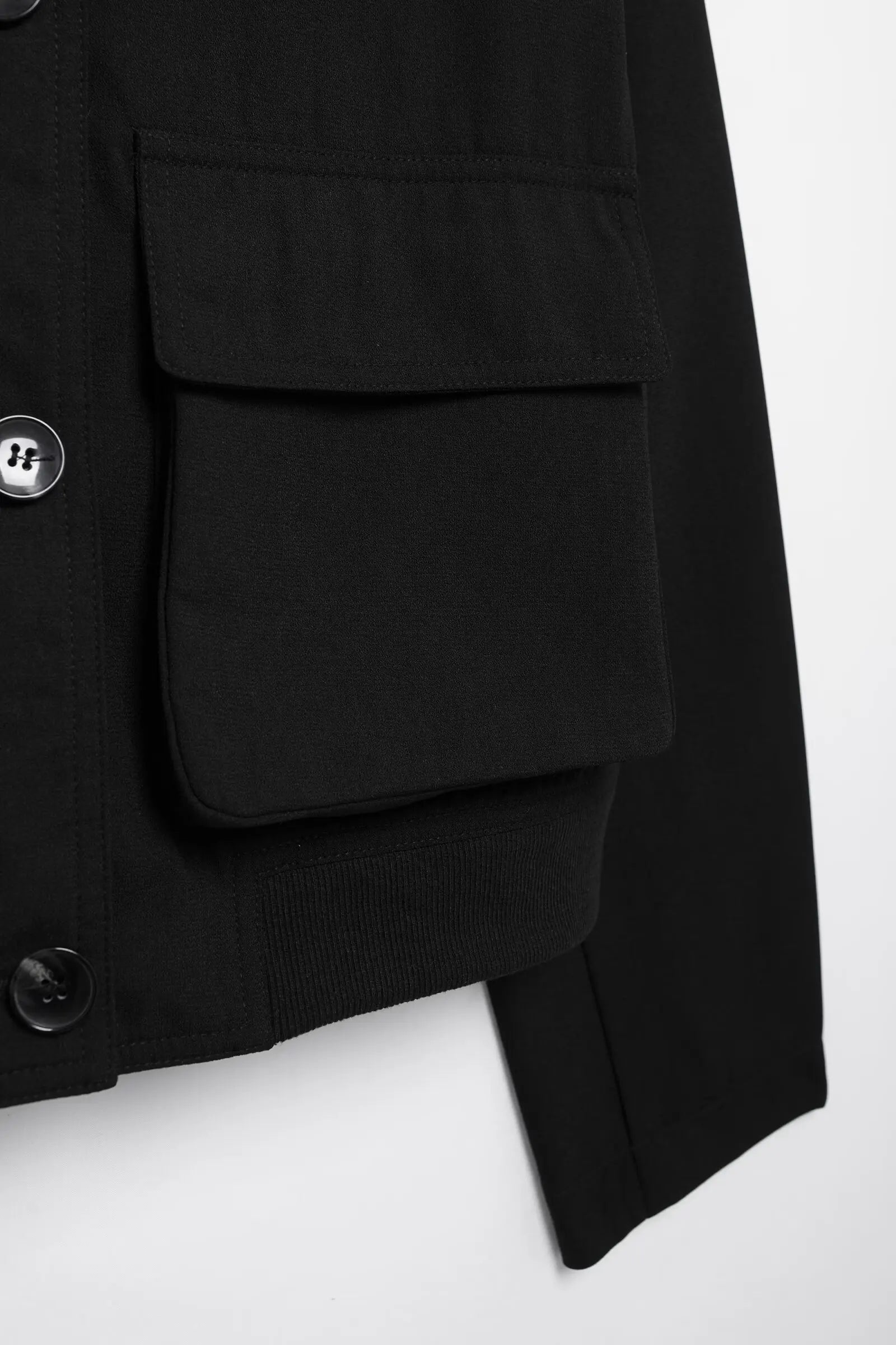 Close-up of a black coat with button details on a white background