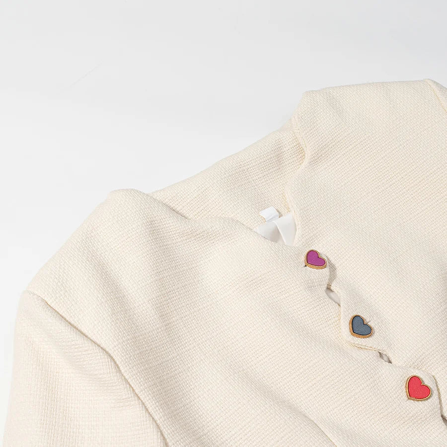 Close-up of a cream-colored garment with colorful heart-shaped buttons on a light gray background