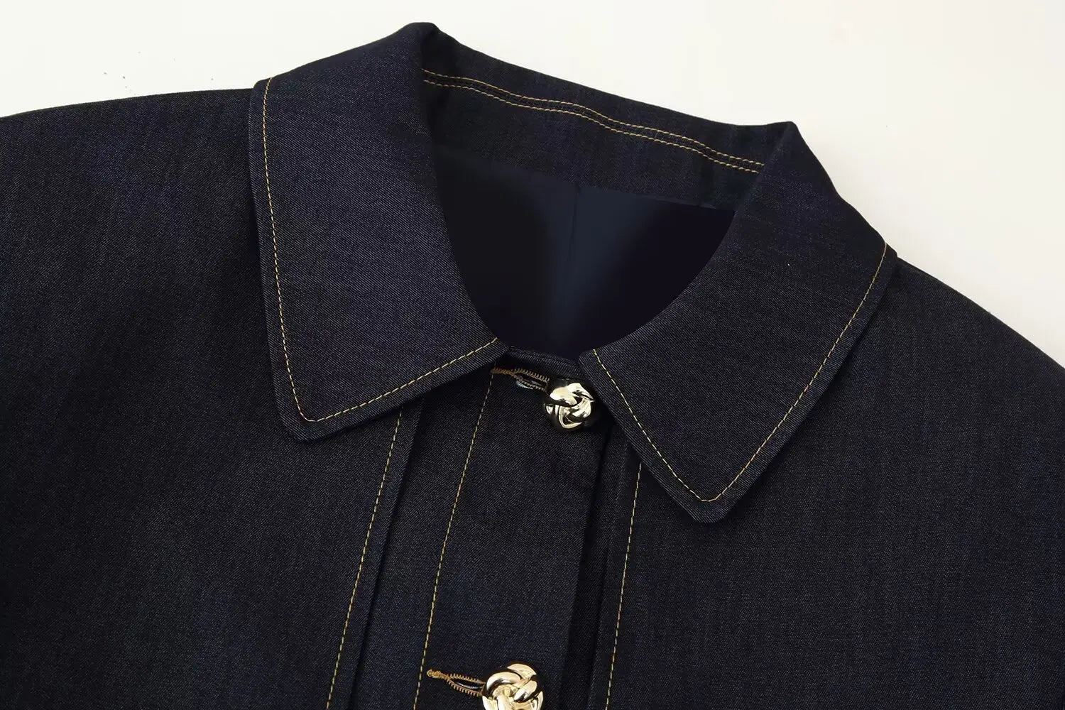 Close-up of a dark blue coat with a collar and gold button on a white background