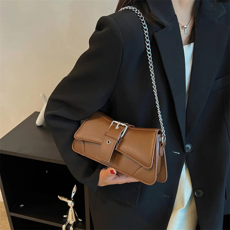 Person holding a brown leather handbag with a chain strap against a neutral background