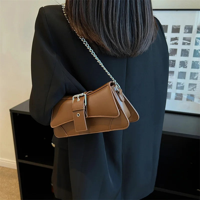 Person holding a brown leather handbag with a chain strap indoors.