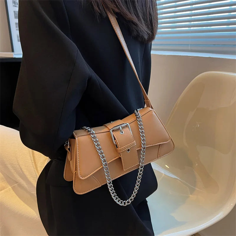 Person wearing a tan handbag with a chain detail in an indoor setting