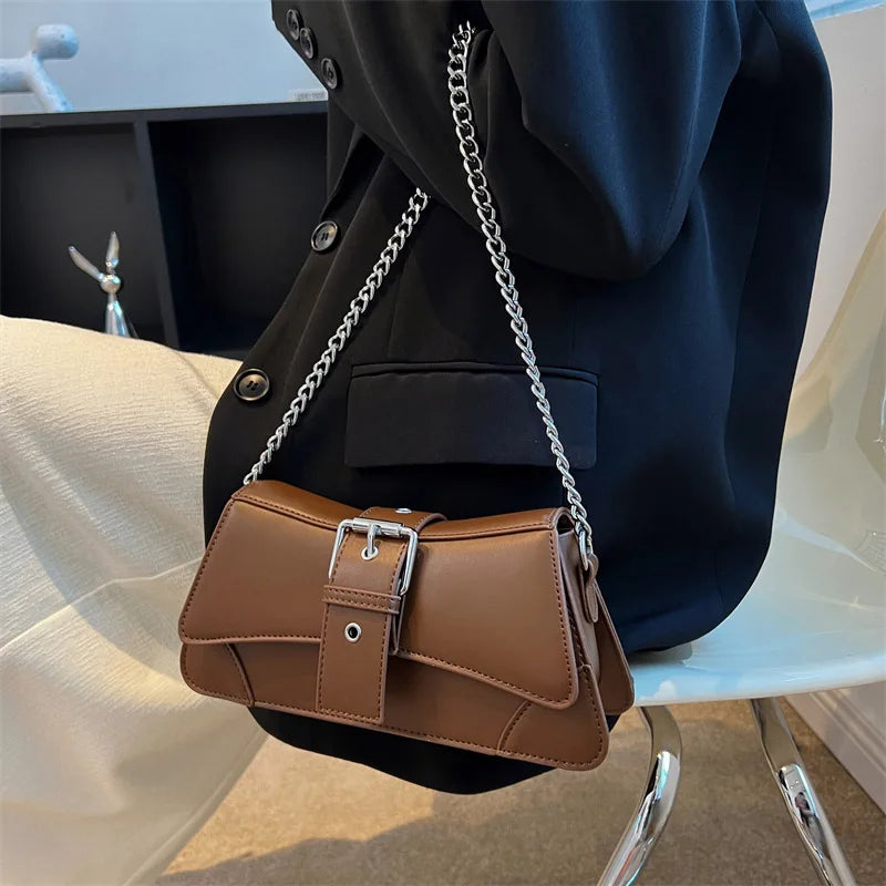 Brown handbag with a chain strap worn by a person sitting on a chair.