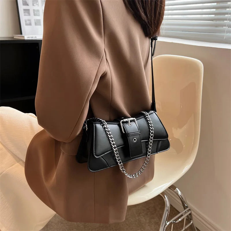 Person wearing a brown coat holding a black handbag with a chain detail.