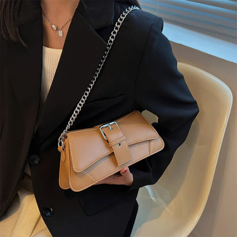 Person holding a tan handbag with a chain strap in an indoor setting