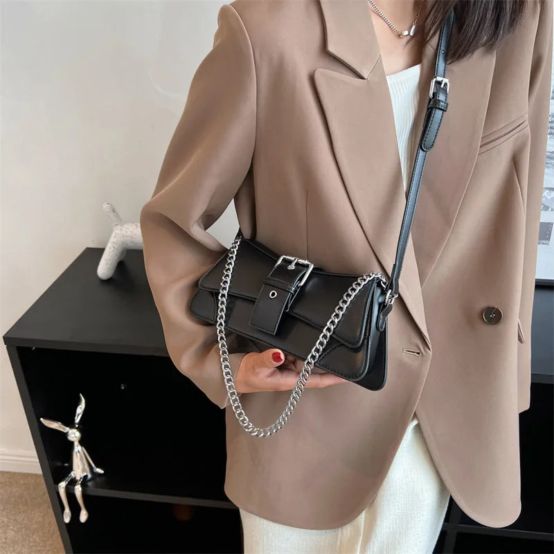 Person wearing a beige blazer holding a black handbag with a chain strap.