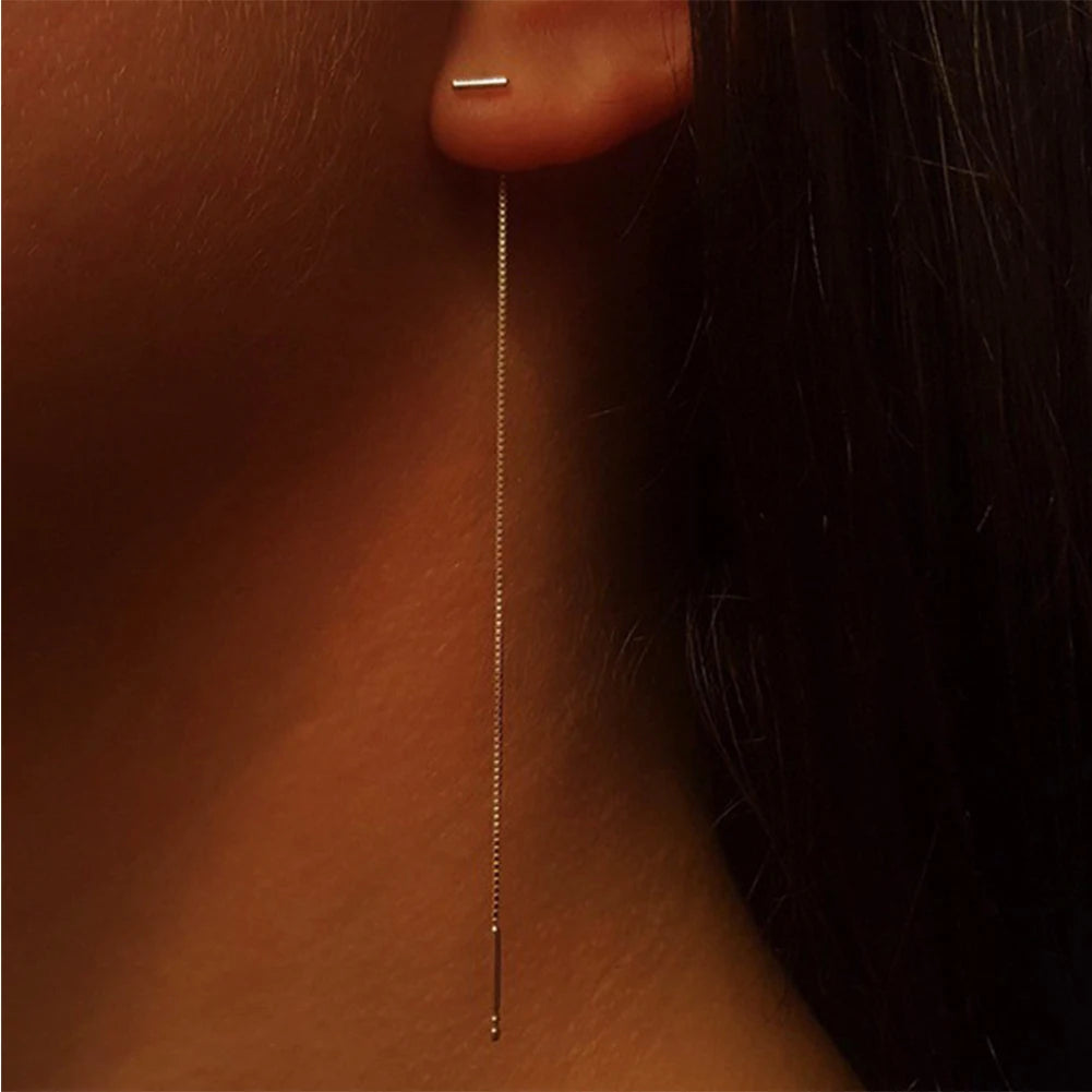 Silver Minimalist Tassel Earrings of a gold threader earring on an ear with a dark background