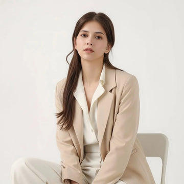 Woman sitting on a chair wearing a beige suit against a white background