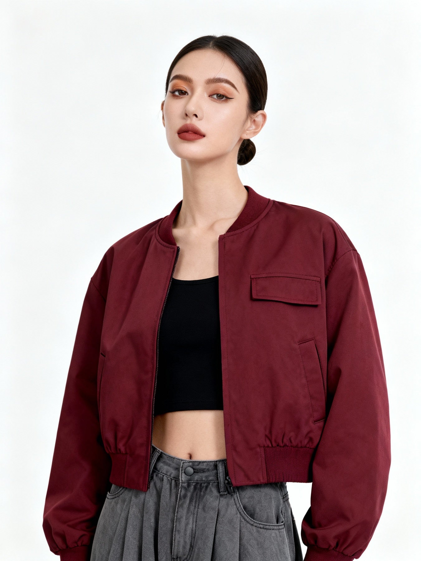 Woman wearing a burgundy jacket over a black top and gray pants on a white background