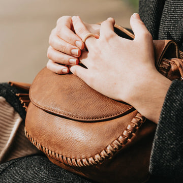 Close-up of hands holding a brown leather bag with a blurred background