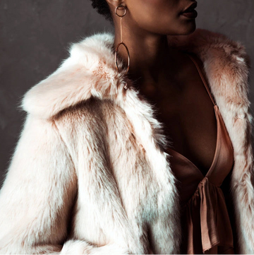 Woman wearing a light pink fur coat against a dark background