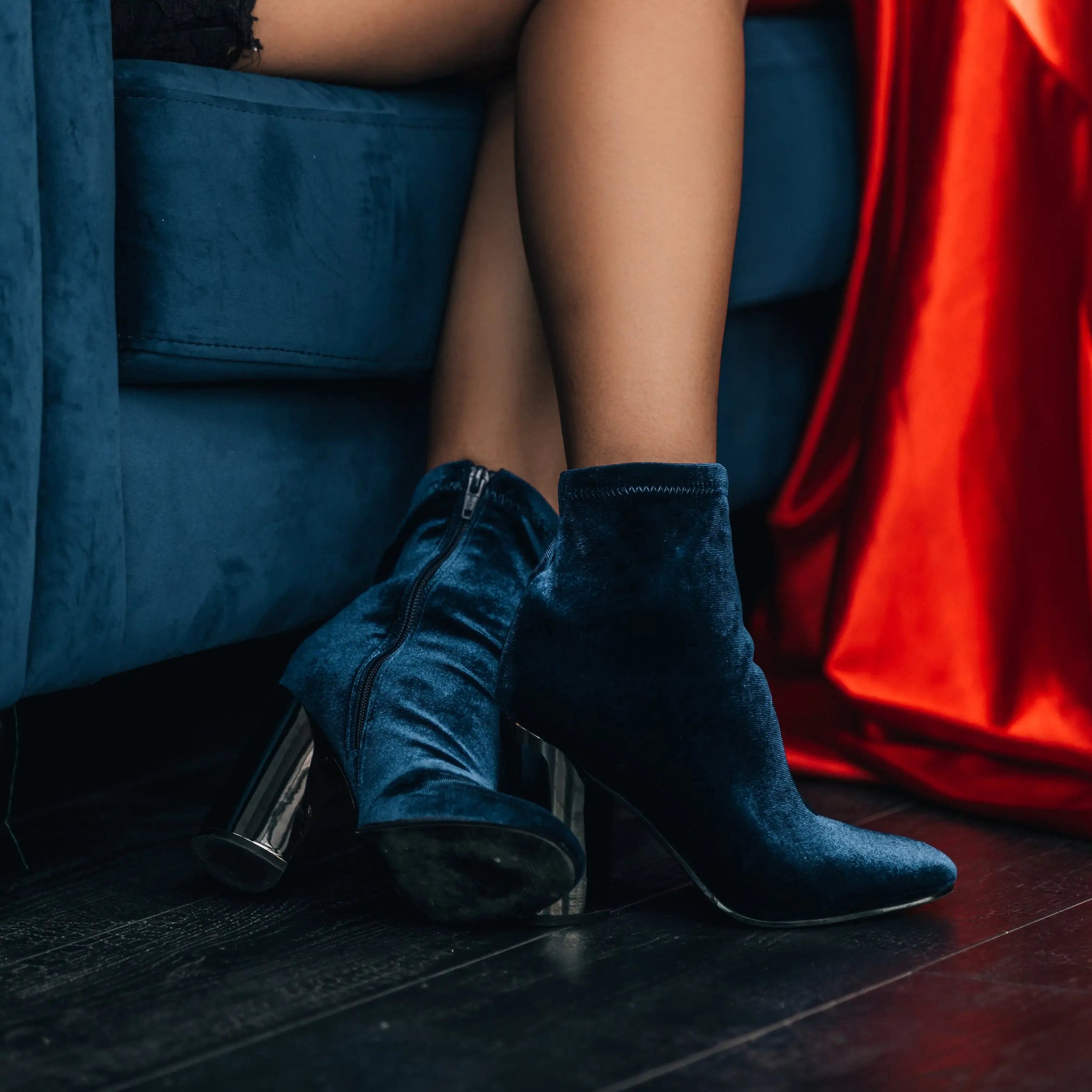 Person wearing blue high-heeled shoes sitting on a blue couch with red fabric.