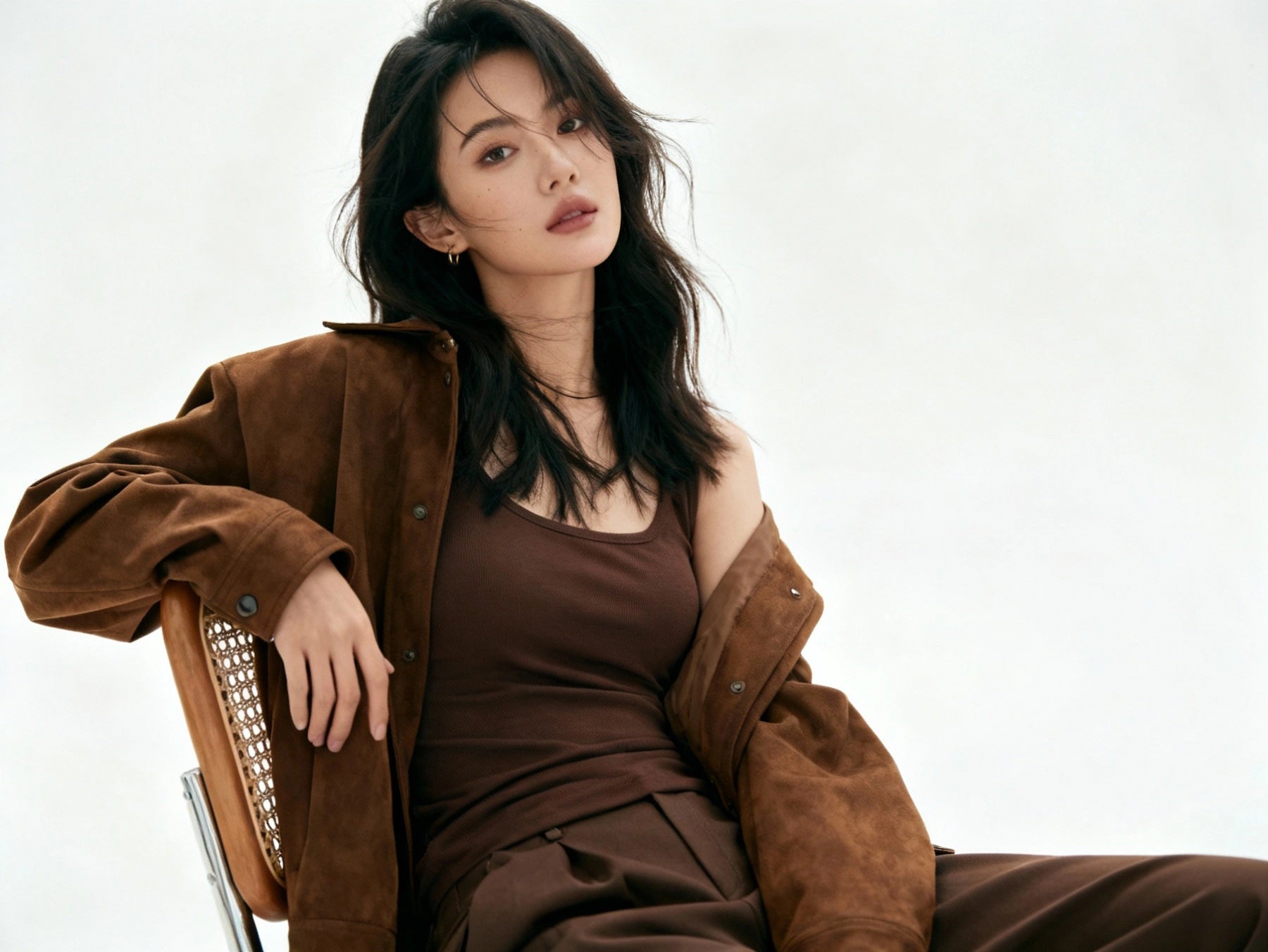 Woman wearing a brown coat and dress sitting on a chair against a white background