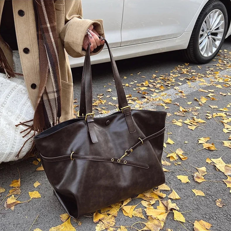 Brown leather handbag on a street with autumn leaves and a car in the background